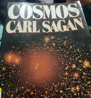 The cover of the Cosmos book- stars and a galaxy, the title, and Sagan's name