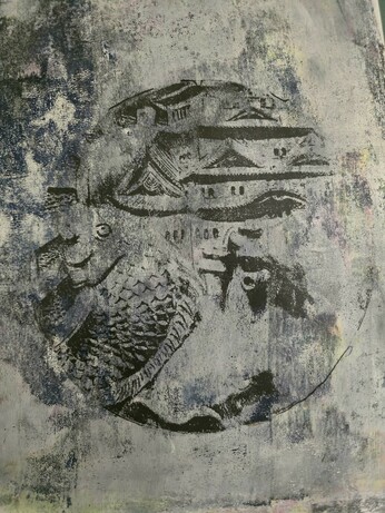 A circular print of a mural sculpture in Himeji depicting a fish and the castle.