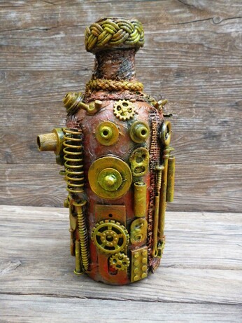 This image features a bottle that has been transformed into a compelling piece of steampunk-style art. Dominating the scene, the bottle is intricately adorned with an assortment of small mechanical components—gears, springs, bolts, and screws—all arranged with meticulous care. These metallic elements, some brass-colored and others with a more muted, rust-toned patina, create a textured and tactile surface that invites closer inspection.

The bottle itself shows a warm, earthy base color beneath the metallic embellishments, blending hues of orange, brown, and copper. This color palette enhances the antique and industrial vibe typical of the steampunk aesthetic. The bottleneck is wrapped in a thick, woven cord that adds a rustic yet deliberate finish to the piece, giving it a handcrafted feel. The backdrop, a rough wooden surface with visible grain, contrasts with and highlights the bottle's mechanical intricacies, grounding the artwork in a natural, raw environment.

Artistically, this creation evokes themes of invention and the fusion of organic and mechanical life, hallmarks of the steampunk genre, which melds 19th-century industrial steam-powered machinery with fantasy or speculative technology. Symbolically, this transformation of a mundane bottle into a miniature machine-like relic could suggest ideas about recycling, the beauty of repurposing objects, or the potential for hidden complexity within the everyday.
