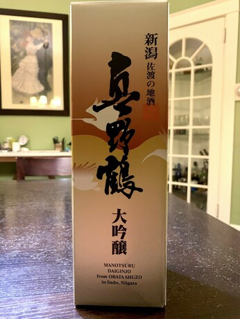 A box containing a sake bottle, featuring Chinese characters that include its name, Manotsuru, and its grade, Daiginjo.