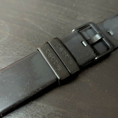 Auto-generated description: A black watch strap features the word pebble engraved on a loop.