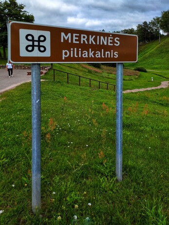 A sign for the Merkinė hill fort, with the Apple Mac command sign.