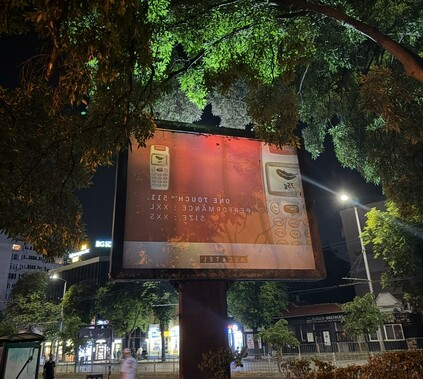 A billboard in a city at night. It faintly displays an ad for a mobile phone from the year 2002.