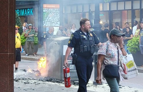 Big Belly trash compactor thing on fire, as Transit PD cop walks away with extinguisher