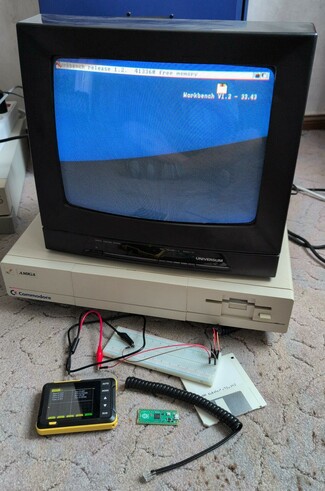 Amiga 1000 with a CRT TV connected, workbench loaded. Breadboard, osci, Raspi pico, floppy