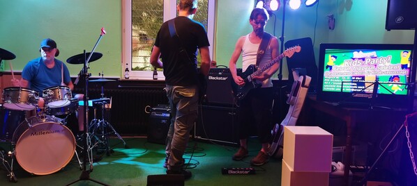 Ein Bild unseres Bühnenbereichs mit drei Musikern die Musik spielen.