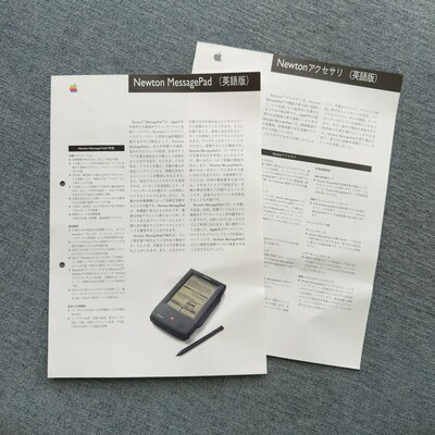 A pair of Japanese language documents are staggered on top of each other. The text contains descriptions, specifications, and other information pertaining to Apple’s original Newton MessagePad PDA and various accessories available for the system. Both documents are printed primarily in black and white. The topmost document has a rainbow Apple logo in the top left corner and a colour photo of the MessagePad device on the bottom right of the page.