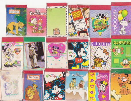 La foto muestra 18 portadas de libretas pequeñas con distintos personajes, la mayoría de Disney como El rey león o el Ratón Mickey. También está presente Snoopy, Hello Kitty y otros.