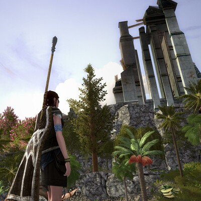 A screenshot from LOTRO, showing a roughly-clothed woman  carrying a spear on her back, standing not far from a tall crag with part of a ruin on top. The crag appears unclimbable and has various palms and other trees at its base.