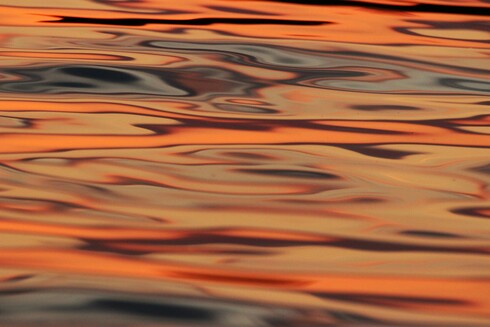 Photograph of sunset light on still lake water, creating swirls of orange, green, blue, and purple.