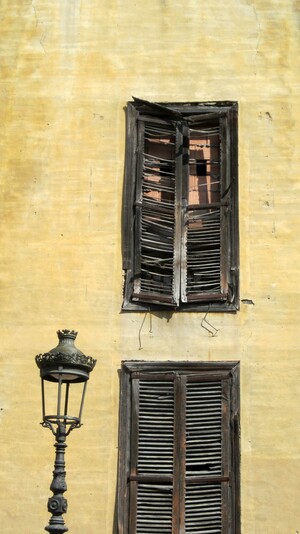 Fotografía en color de una farola frente a una pared con dos ventanas tapiadas a la luz del sol