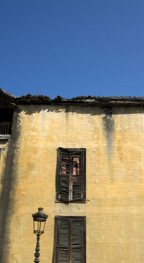 Fotografía en color de una farola frente a la pared de una casa abandonada cuyas ventanas están tapiadas
