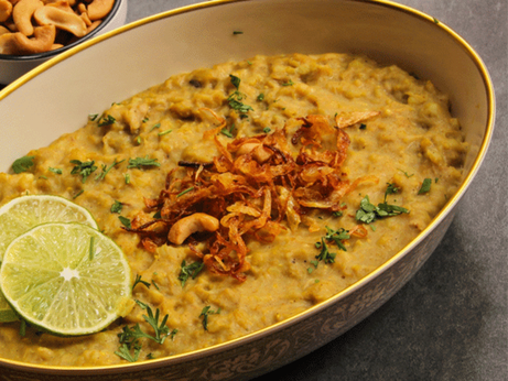 A picture of haleem, which is a yellow-orange stew with limes and other toppings on it.
