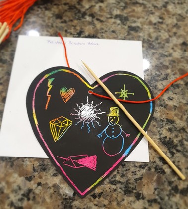 A little kit with a heart-shaped black piece of paper and a thin, sharp stylus. The black layer on top of the heart scrapes away to reveal rainbow colors, allowing the kids to decorate their hearts. This one is decorated with various pictures like a snowman and a bolt of lightning.