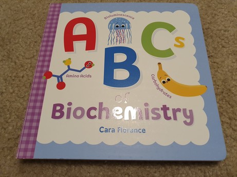 A book called "ABCs of Biochemistry". The A is a molecule labeled Amino Acids, the B is a jellyfish labeled bioluminesence, the C is a banana labeled "carbohydrates".