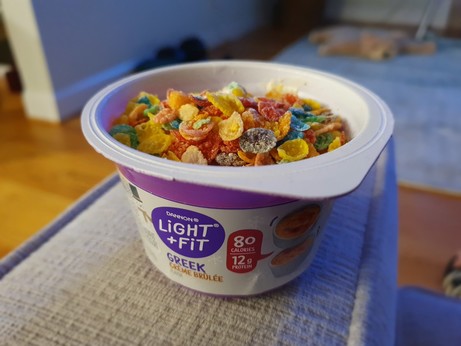 A cup of creme brulée Greek yogurt with fruity pebbles in it.