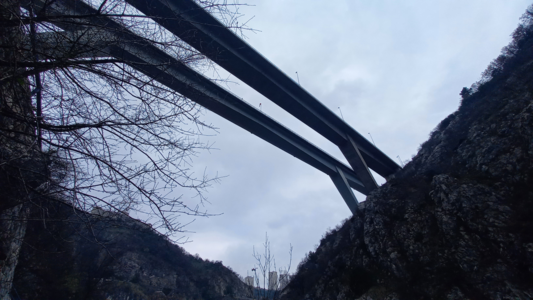 Underneath the highway with a few big buildings visible in the distance.