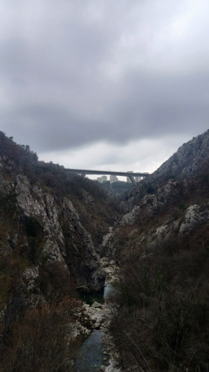 The highway (bridge) in the distance and the river underneath it. A part of the city is visible in-between the ravine's butt cheeks.