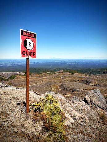Danger cliff sign in front of volcanic landscape with volcano at horizon