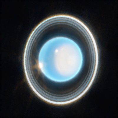 The planet Uranus on a black background. The planet appears light blue with a large, white patch on the right side. On the edge of that patch at the upper left is a bright white spot. Another white spot is located on the left side of the planet at the 9 o’clock position. Around the planet is a system of nested rings. The outermost ring is the brightest while the innermost ring is the faintest. Unlike Saturn’s horizontal rings, the rings of Uranus are vertical and so they appear to surround the planet. Credits: NASA, ESA, CSA, STScI. Image processing: J. DePasquale (STScI)