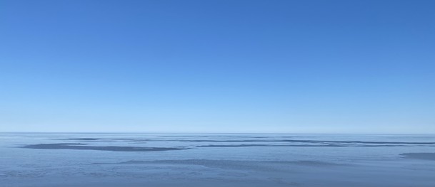 Looking northwest over Lake Sperior, blue sky, white-ish lake with patches of blue where this ice is melted. 