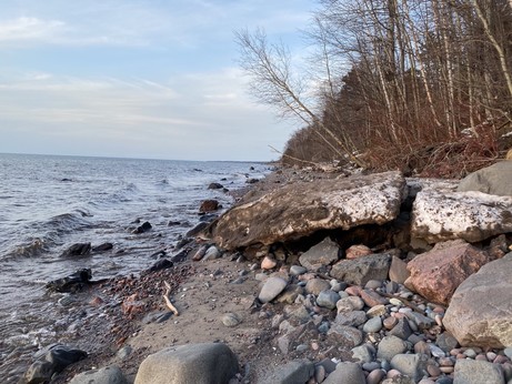 Lake Superior to the left, looking down a rocky beach.
Large chunk of dirty ice on top of the rocks.
Bank with bare trees on the right.