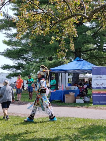A dancer in full regalia strides toward the stage. 