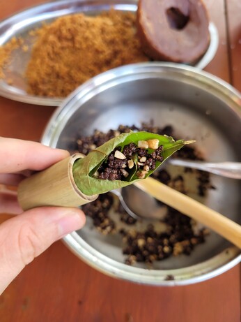 Un segment de bambou tenu entre deux doigts, dans lequel une  feuille d'arbre est roulée, pour contenir un mélange de pâte de cacao et cacahuètes. 