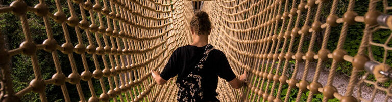 Persons walking very high up inside a cargo netting corridor like a tunnel walking from one valley to another.

A metaphor for contact and communicate with each other by slowly talking / walking together even though it seems full of problems... 

Picture is about Trust.

Hashtag #FreeSchool for more